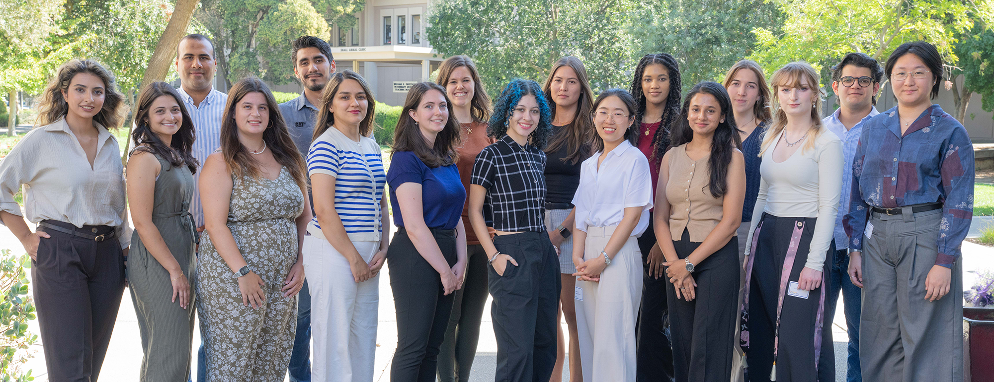 A group of people standing outside with green trees behind them.