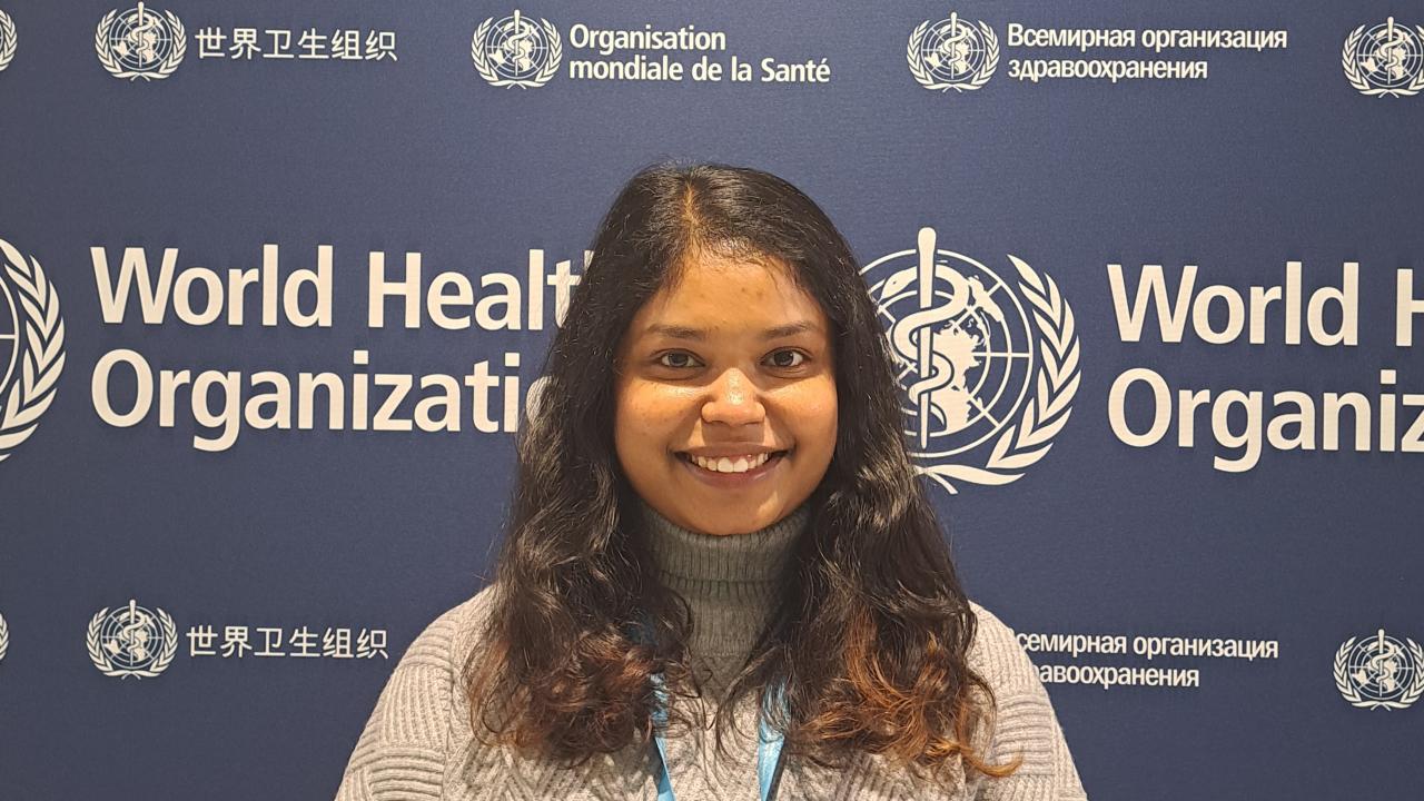 Jahnavi Akula stands in front of a banner with World Health Organization branding