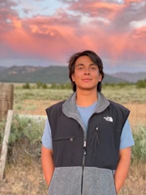 Person smiling in front of sunset and mountain.