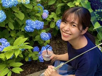 Person smiling in front of flower bush.
