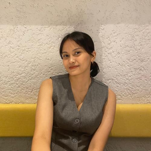 Person sitting and smiling in front of a wall.