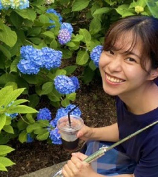 Person smiling in front of flower bush.