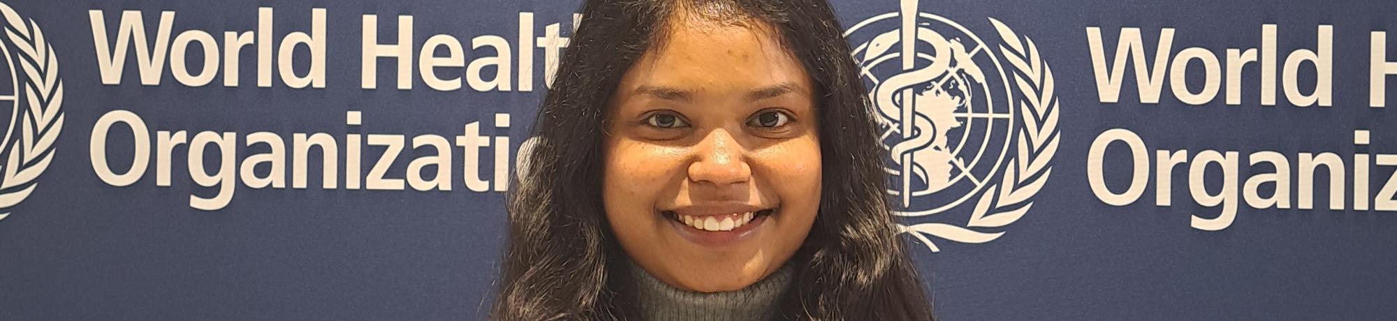 Jahnavi Akula stands in front of a banner with World Health Organization branding